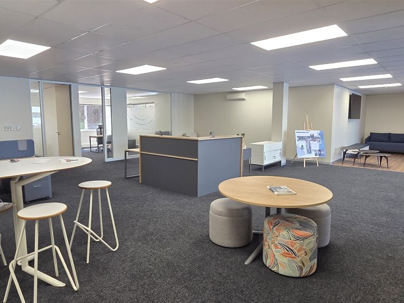 Spacious open-plan office area featuring modern glass partitioning, suspended ceilings with recessed lighting, and neutral carpet flooring throughout.
