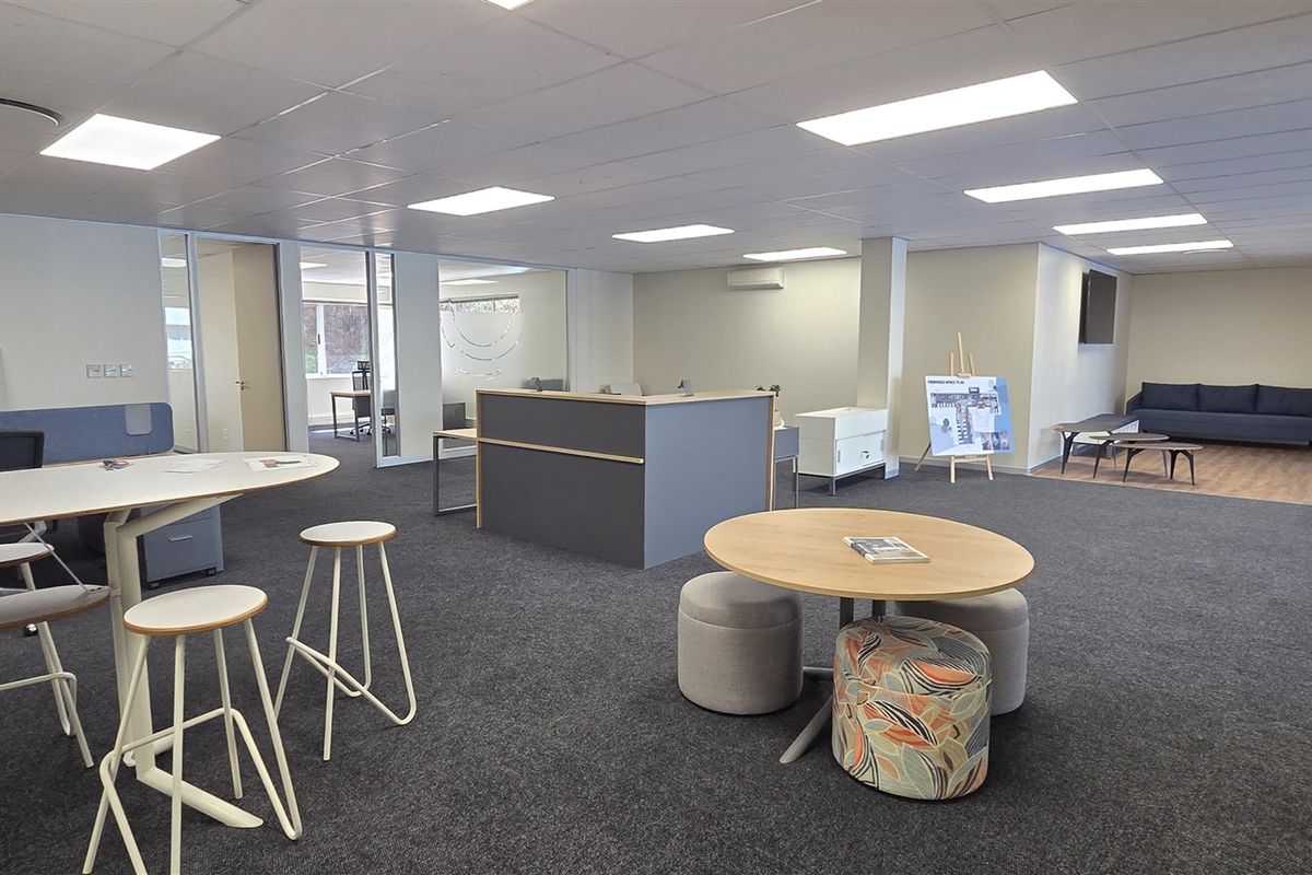Spacious open-plan office area featuring modern glass partitioning, suspended ceilings with recessed lighting, and neutral carpet flooring throughout.