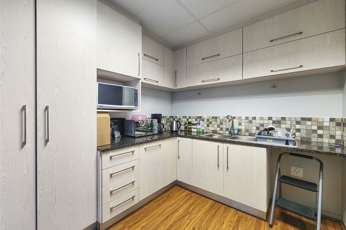 A functional office kitchenette featuring light wood-grain cabinetry, granite countertops, a mosaic tile backsplash, and integrated microwave space.