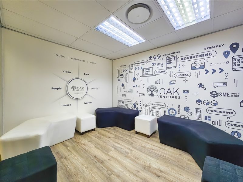 A modern office reception or breakout area featuring branded wall graphics, recessed ceiling lighting, and durable laminate flooring.