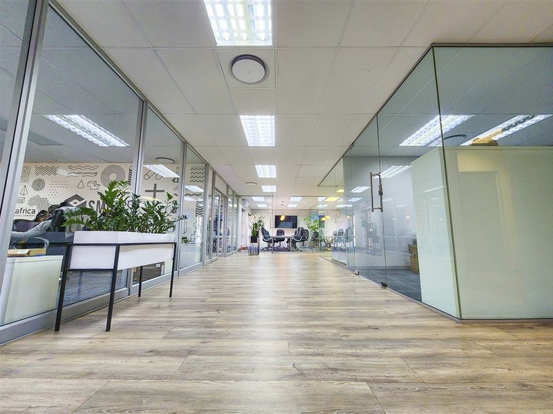 Modern office interior featuring glass partition walls, suspended ceilings with recessed lighting, and durable wood-look flooring, creating a bright and professional workspace.