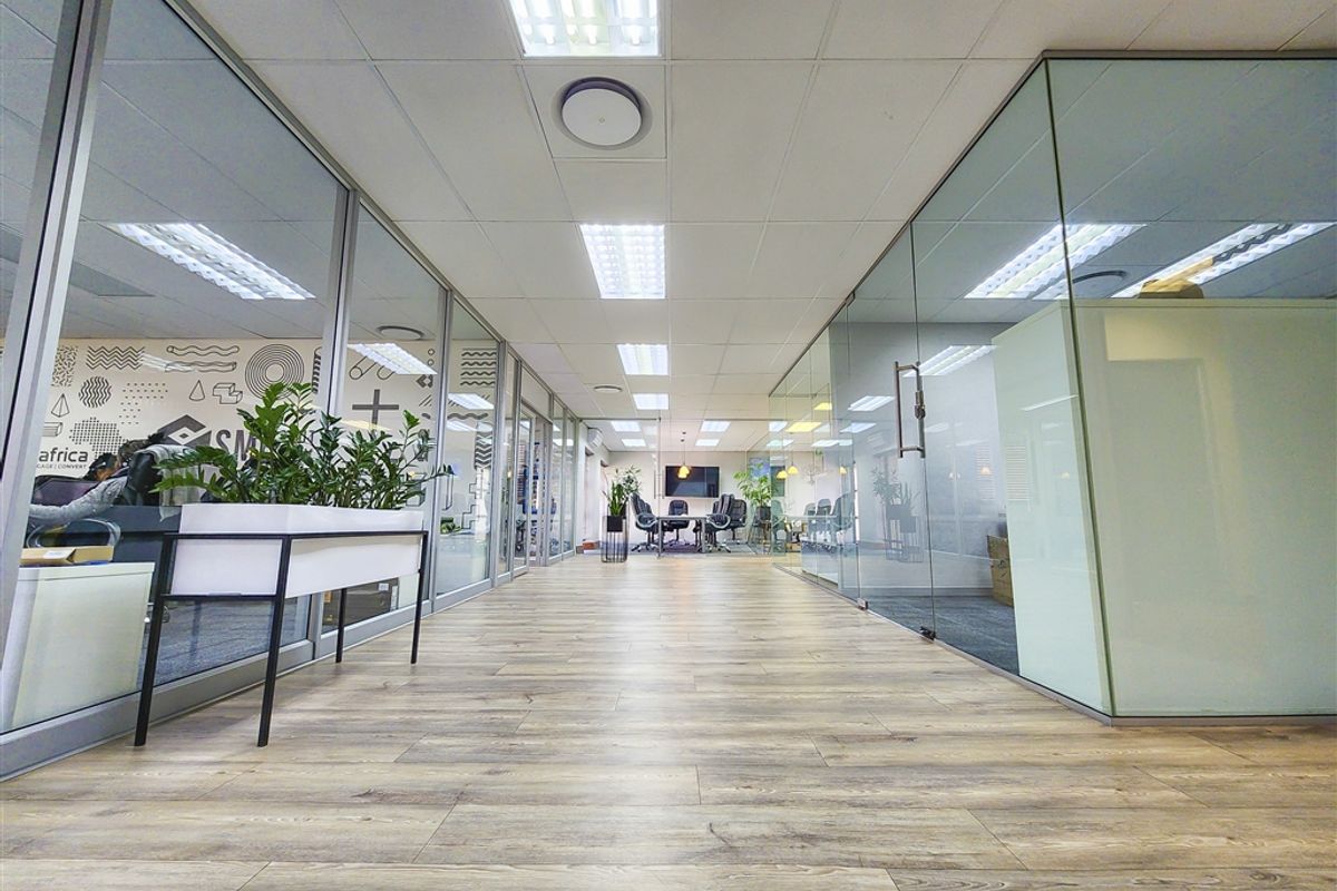 Modern office interior featuring glass partition walls, suspended ceilings with recessed lighting, and durable wood-look flooring, creating a bright and professional workspace.