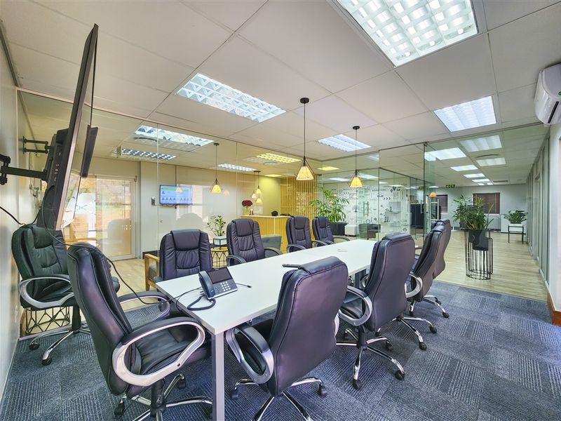 A professional office boardroom featuring glass partition walls, suspended ceilings with recessed lighting, and carpeted flooring, providing a modern and functional workspace.
