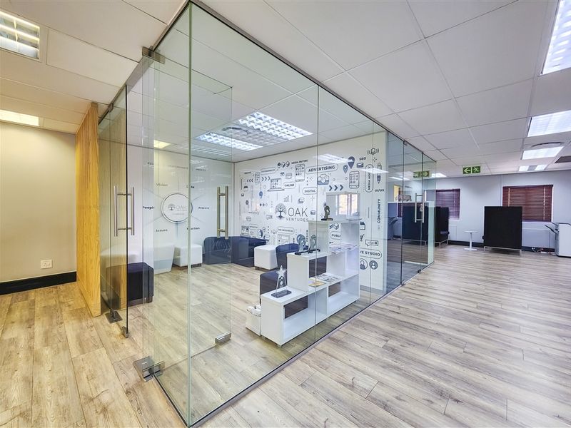 Modern office space featuring glass-partitioned meeting rooms, wood-look laminate flooring, and a clean, professional suspended ceiling design.