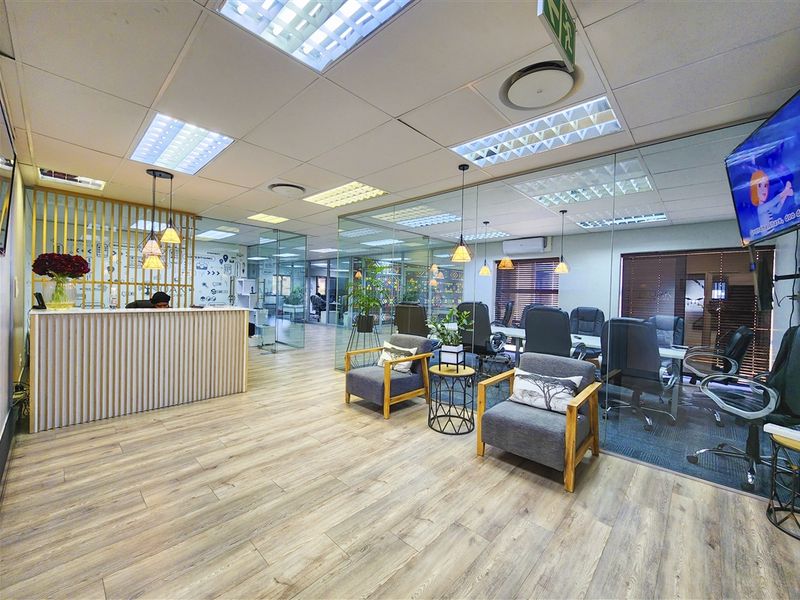 Modern office reception area featuring glass partitioning, laminate flooring, recessed lighting, and a professional reception desk.