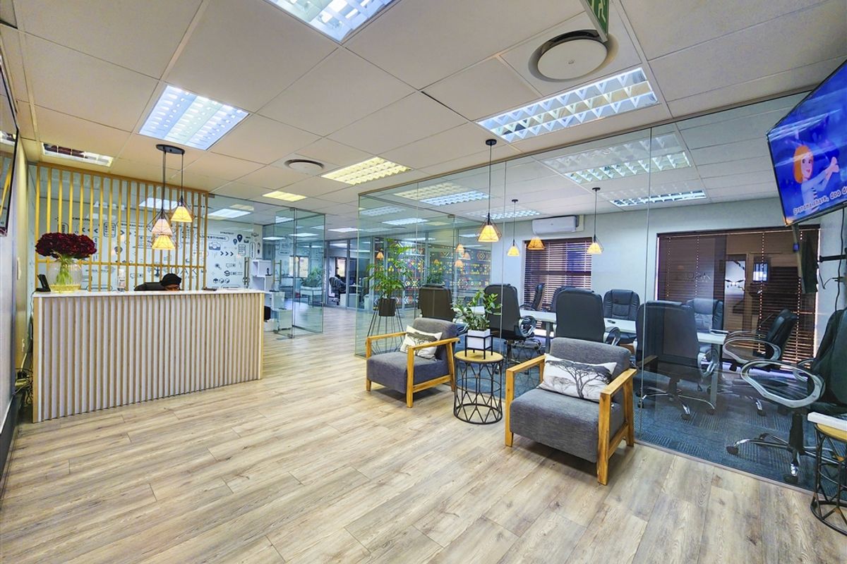 Modern office reception area featuring glass partitioning, laminate flooring, recessed lighting, and a professional reception desk.