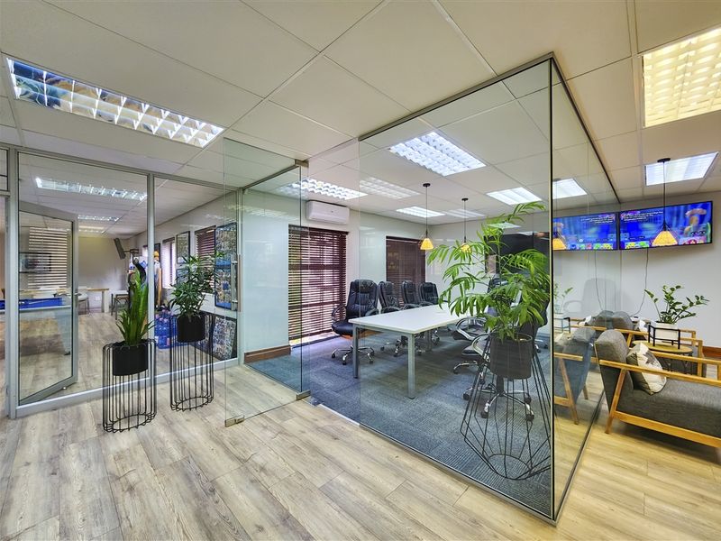 Modern office space featuring glass partition walls, suspended ceilings with recessed lighting, and a combination of carpet and wood-look laminate flooring.