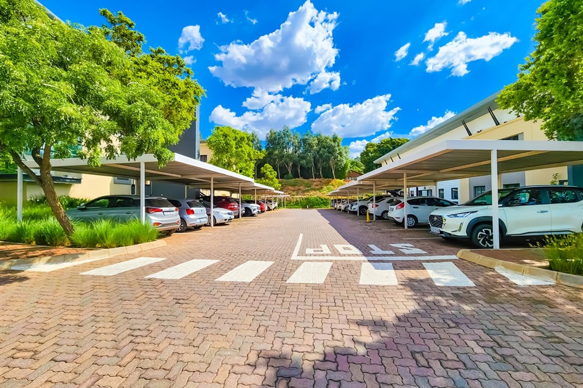 A well-maintained office parking area featuring paved surfaces and multiple covered parking bays surrounded by mature trees.