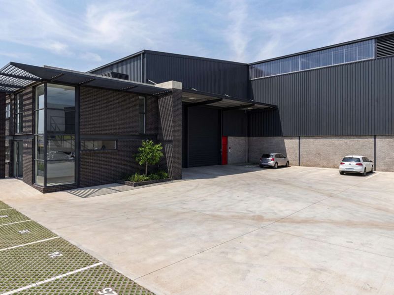 Modern industrial facility featuring a combination of dark brick and metal cladding, large roller shutter door, and dedicated concrete parking area.