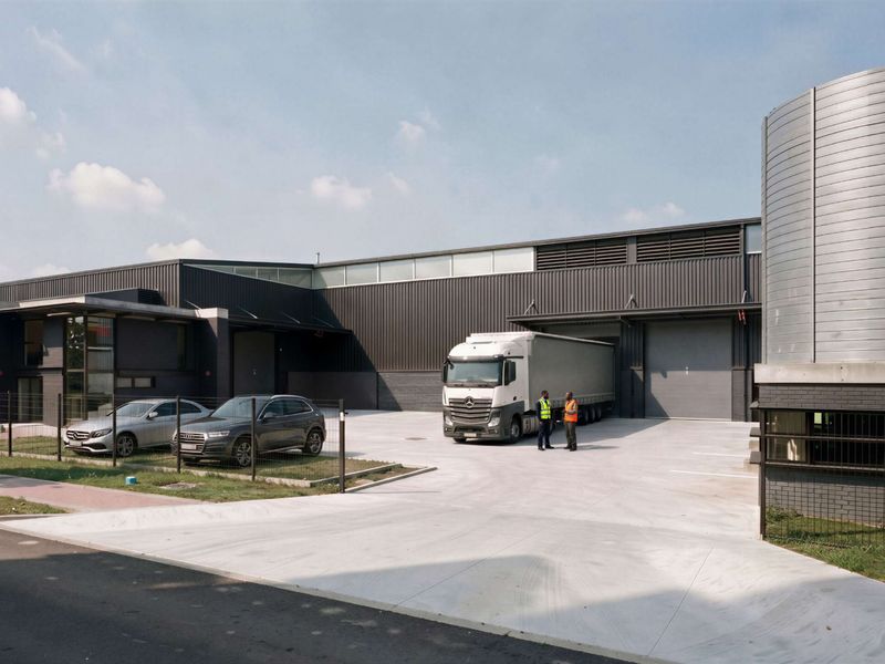 Modern industrial facility featuring metal cladding, large roller shutter loading doors, a concrete yard, and an integrated silo structure.