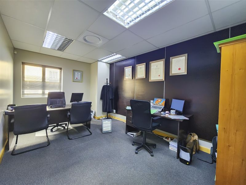 A functional office space featuring a suspended ceiling with recessed lighting, carpeted flooring, and a window with fitted blinds.
