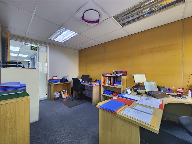 A functional office space featuring a suspended ceiling with recessed lighting, carpeted flooring, and a partition wall, providing a professional work environment.