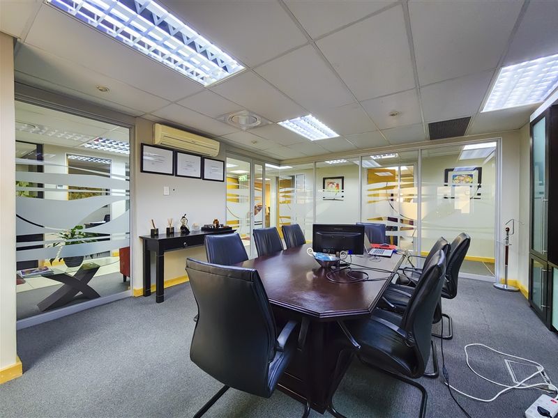 A professional office meeting room featuring glass partitions, suspended ceilings with recessed lighting, and carpeted flooring.