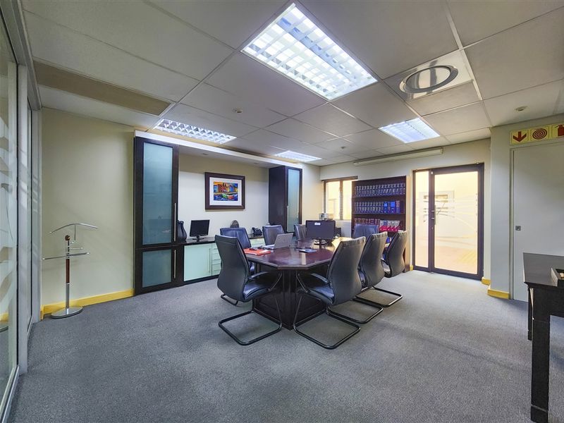 A professional office space featuring a central meeting table, built-in storage cabinetry, suspended ceiling with recessed lighting, and carpeted flooring.