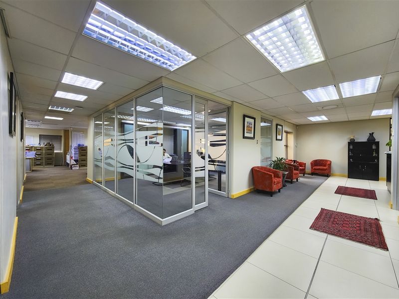 Professional office space featuring glass-partitioned private offices, suspended ceilings with recessed lighting, and a combination of carpet and tiled flooring.