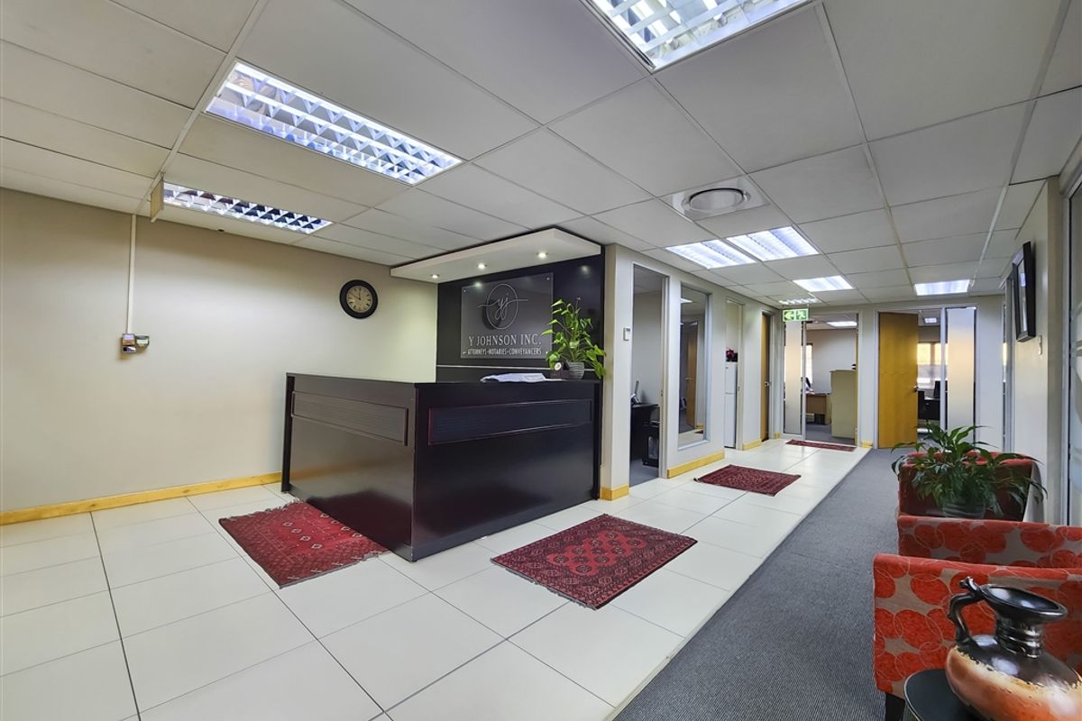 Professional office reception area featuring a built-in reception desk, suspended ceiling with integrated lighting, and a combination of tiled and carpeted flooring.