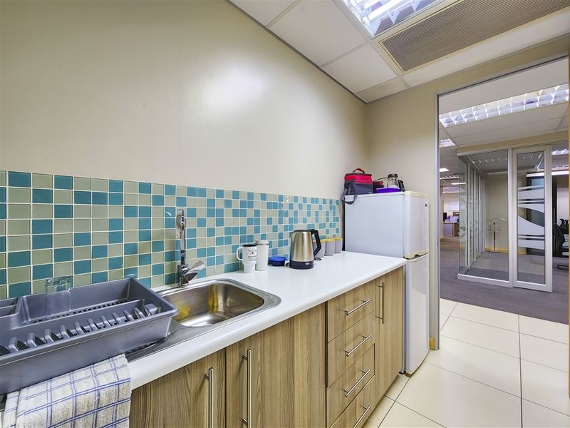 A compact office kitchenette featuring laminate cabinetry, a stainless steel sink, a vibrant tiled backsplash, and durable ceramic floor tiles.