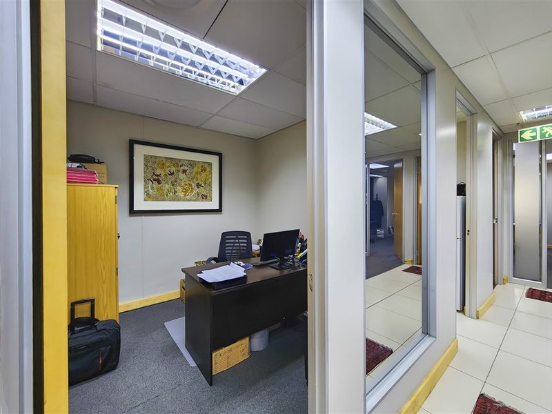 A functional office space featuring a glass partition wall, suspended ceiling with recessed lighting, and a combination of carpet and tiled flooring.