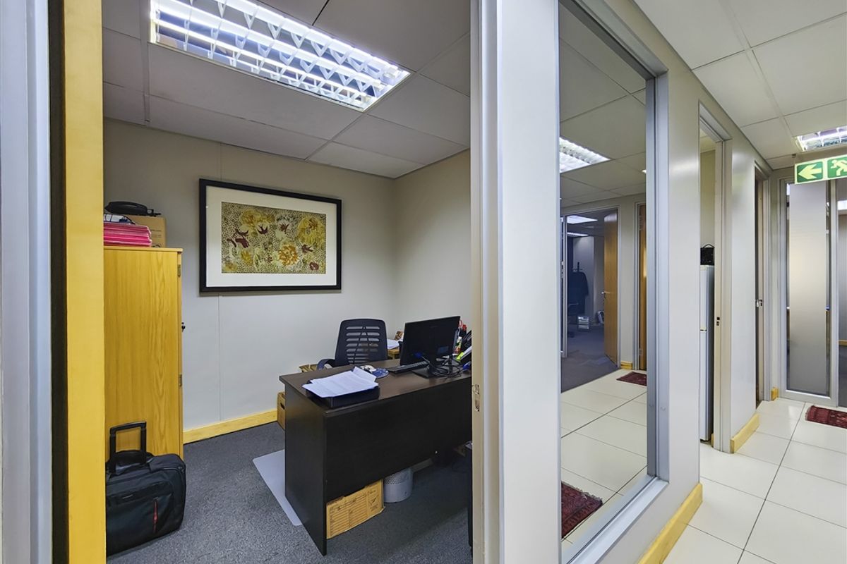 A functional office space featuring a glass partition wall, suspended ceiling with recessed lighting, and a combination of carpet and tiled flooring.