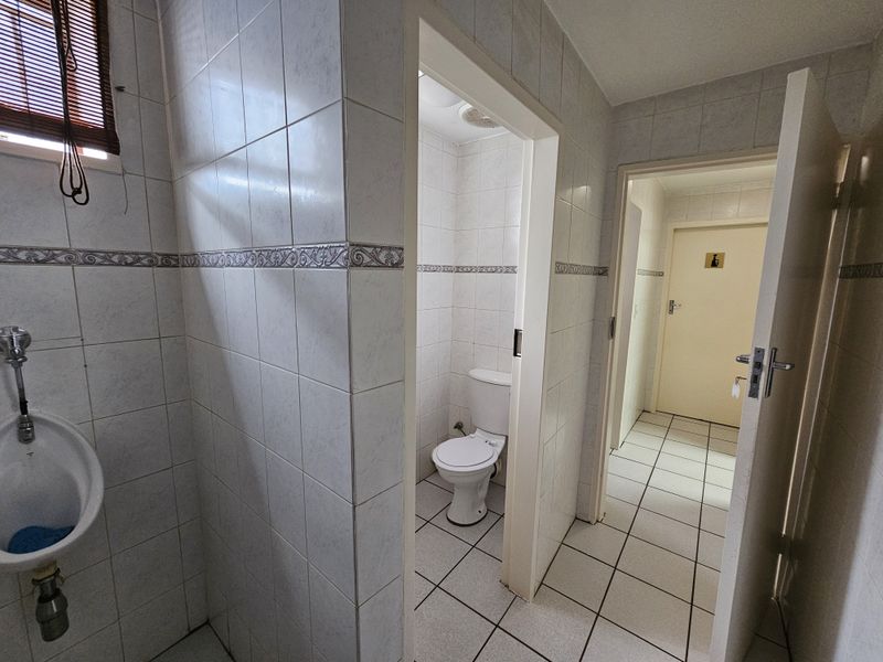 A functional office restroom facility featuring a wall-mounted urinal, a private toilet cubicle, and tiled flooring throughout.