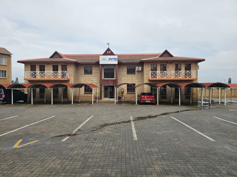 A professional office building featuring a face-brick facade, tiled roof, and covered parking bays with paved driveway access.