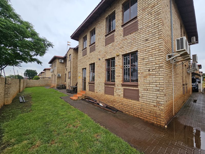 Exterior view of a multi-story brick office building featuring security bars on windows, external air conditioning units, and a surrounding lawn and paved walkway.