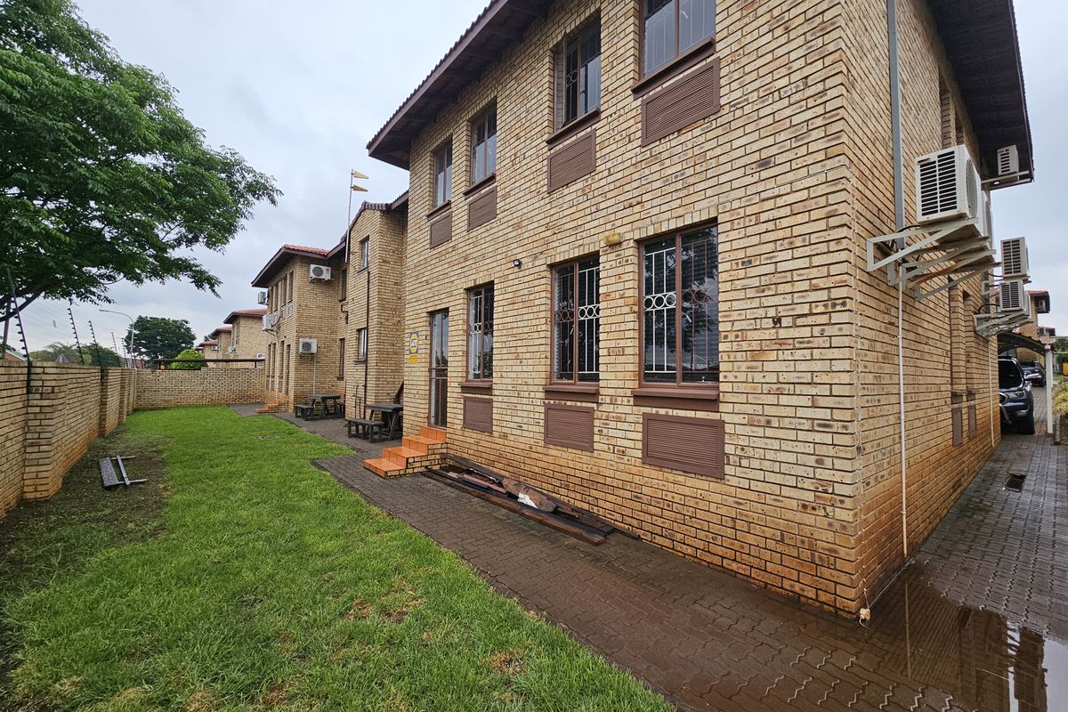 Exterior view of a multi-story brick office building featuring security bars on windows, external air conditioning units, and a surrounding lawn and paved walkway.