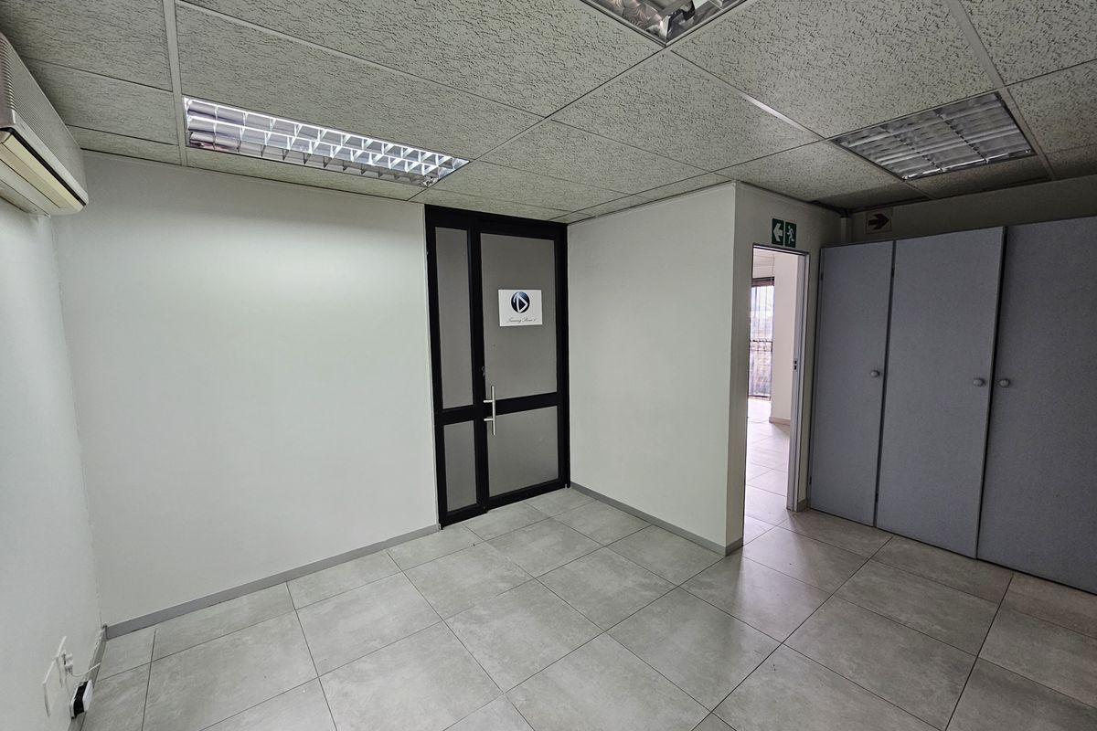 A functional office space featuring tiled flooring, a suspended ceiling with recessed lighting, built-in storage cupboards, and an air conditioning unit.