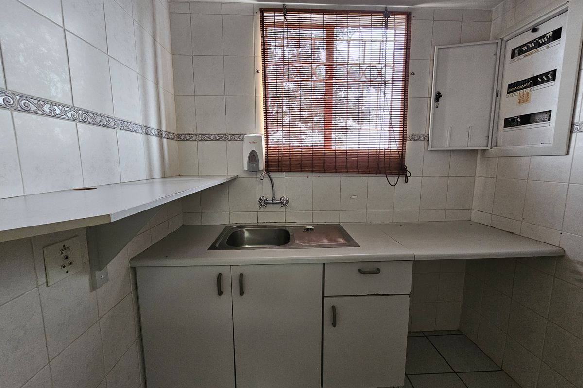 A functional kitchenette area featuring a stainless steel sink, built-in cabinetry, tiled walls, and an integrated electrical distribution board.