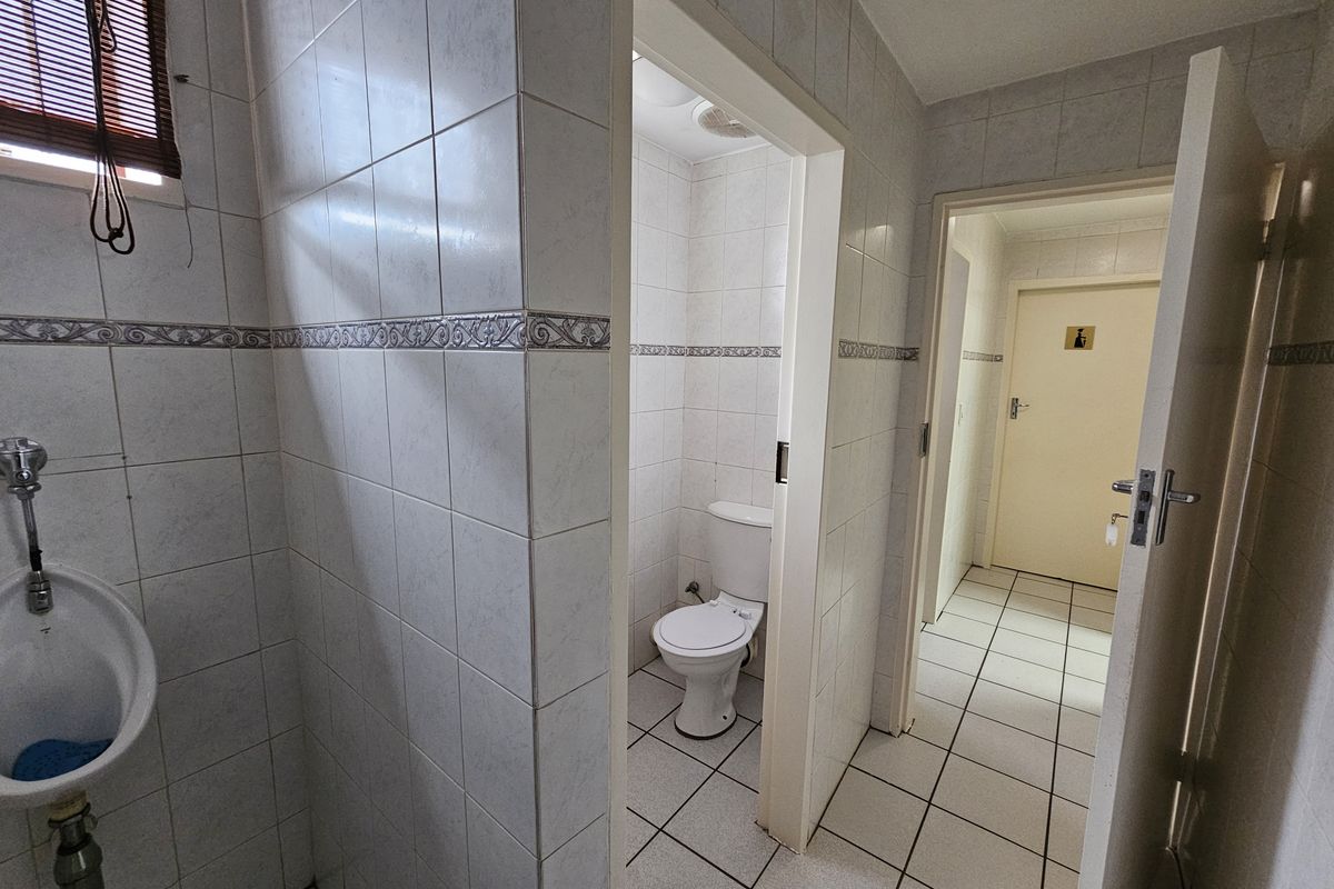 A functional office restroom facility featuring a wall-mounted urinal, a private toilet cubicle, and tiled flooring throughout.