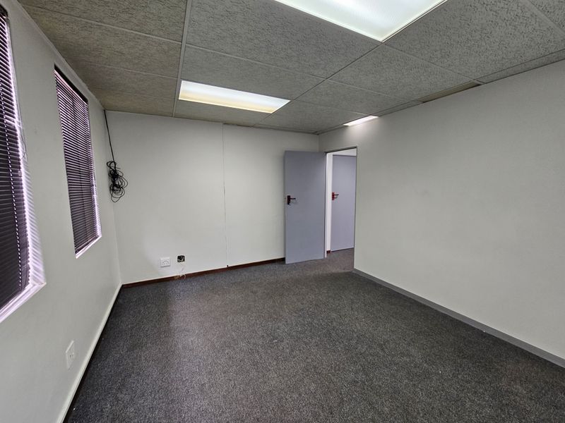A vacant office space featuring grey carpeting, suspended ceiling tiles with integrated lighting, and window blinds.