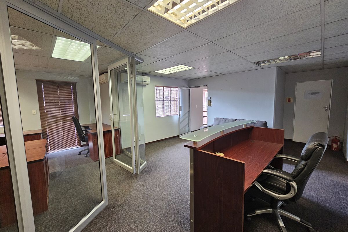Professional office space featuring a reception desk, glass-partitioned private office, carpeted flooring, and recessed fluorescent lighting.
