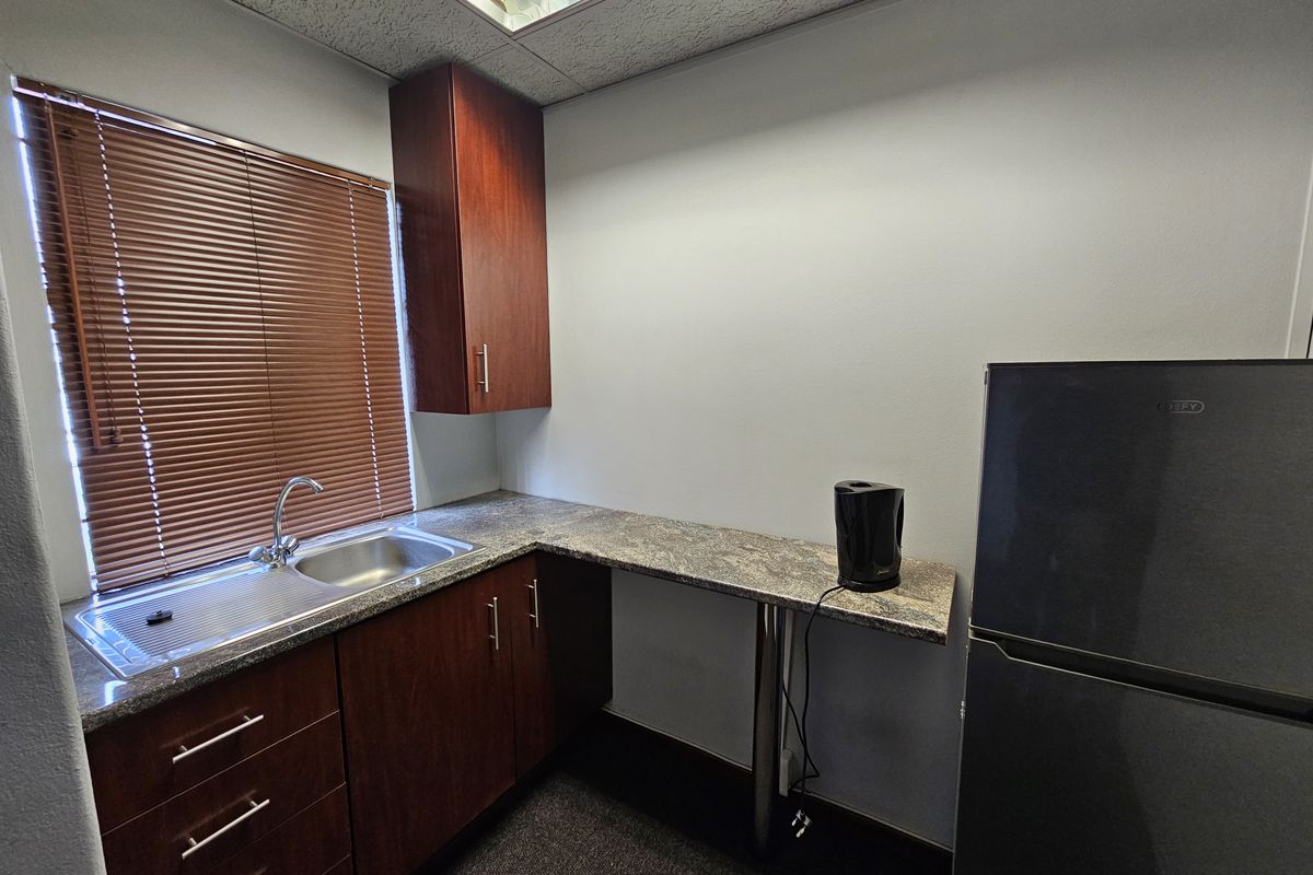A compact office kitchenette featuring dark wood cabinetry, granite-look countertops, a stainless steel sink, and a drop ceiling with integrated lighting.