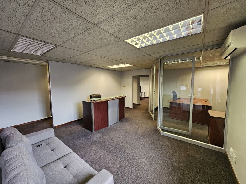 Office reception area featuring a glass-partitioned private office, drop ceiling with recessed lighting, and carpeted flooring.