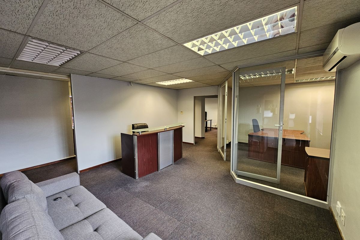 Office reception area featuring a glass-partitioned private office, drop ceiling with recessed lighting, and carpeted flooring.