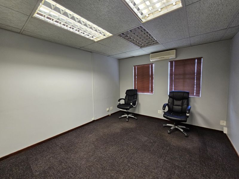 A functional office space featuring a drop ceiling with recessed lighting, wall-mounted air conditioning unit, and carpeted flooring.