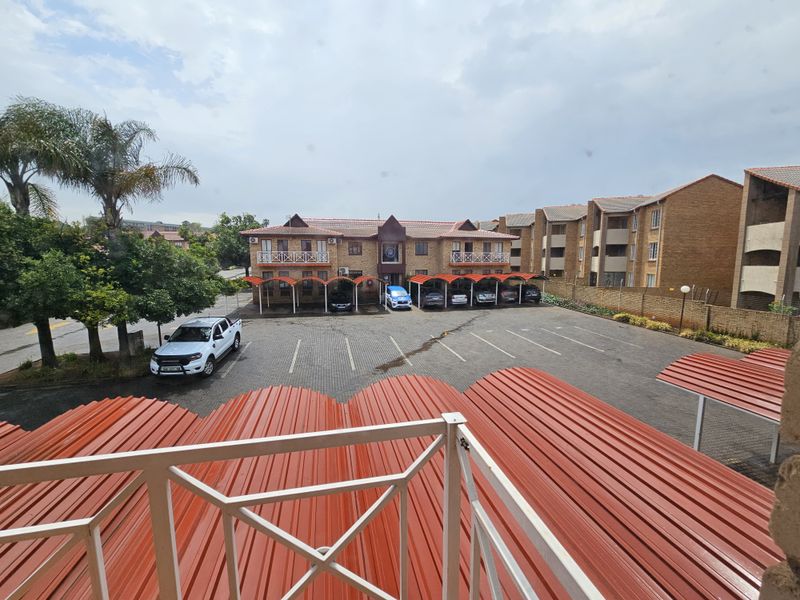 An elevated view of an office complex featuring a paved parking area with covered carports and a multi-story brick building.