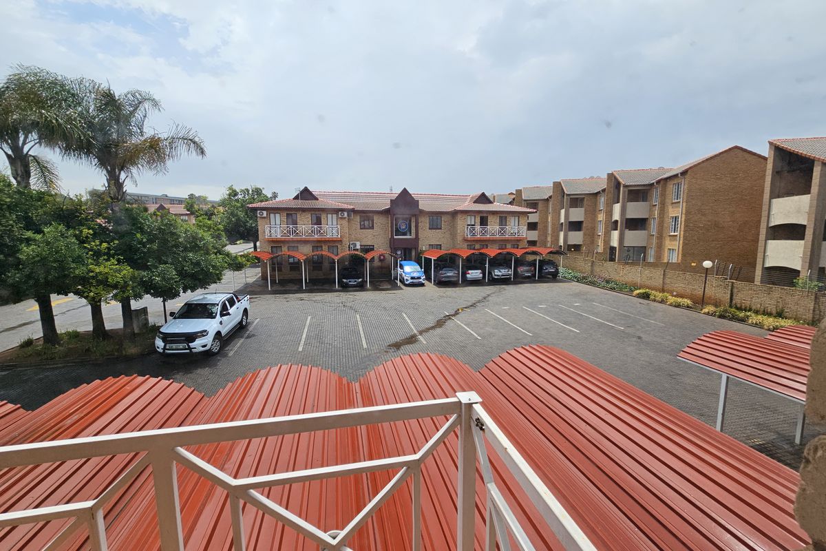 An elevated view of an office complex featuring a paved parking area with covered carports and a multi-story brick building.