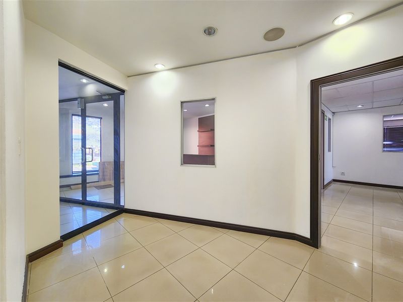 A bright, empty office space featuring ceramic floor tiles, recessed ceiling lighting, and a glass partition wall, offering a clean and professional environment.