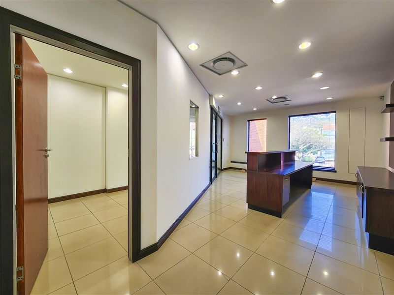 A bright, professional office space featuring tiled flooring, recessed lighting, built-in reception desk, and integrated shelving with large windows providing natural light.