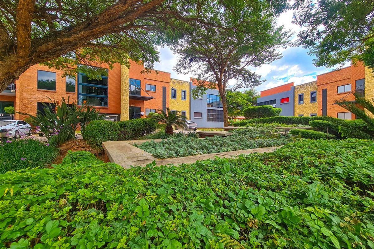 A well-maintained office park exterior featuring landscaped gardens, mature trees, and modern brick and stone building facades.