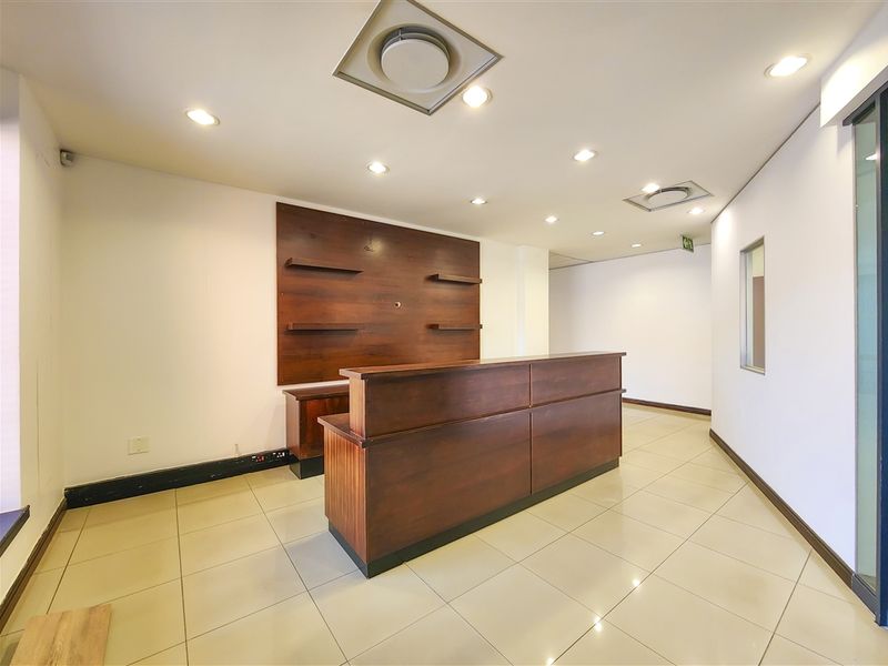 Professional office reception area featuring a built-in wooden reception desk, tiled flooring, and recessed ceiling lighting.