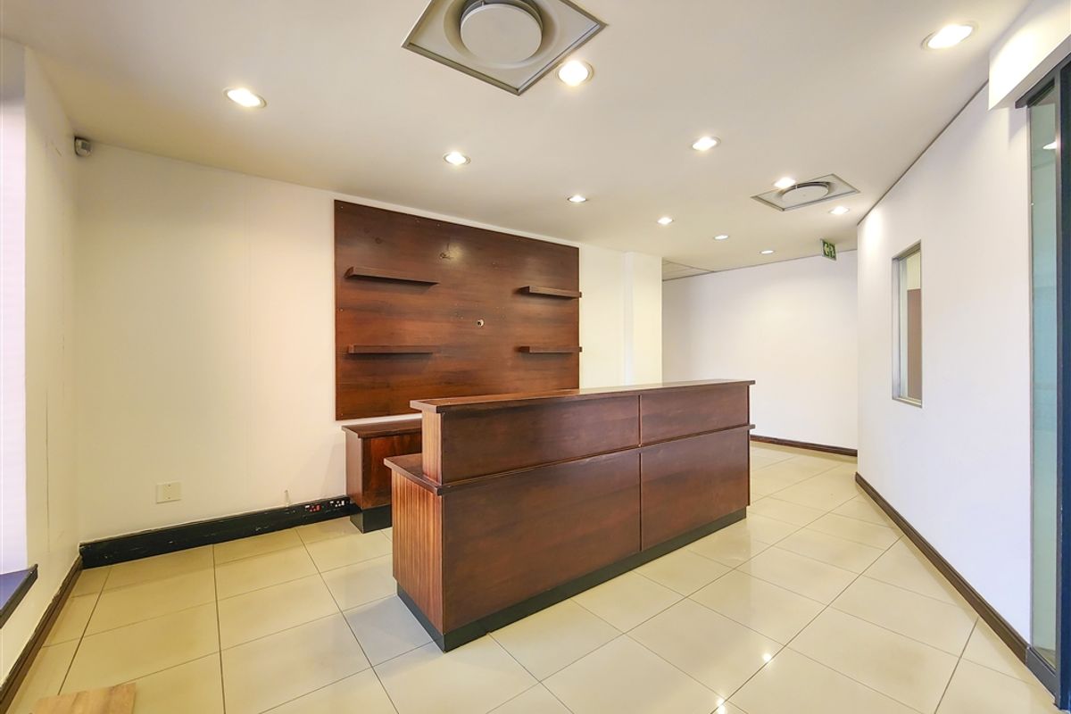 Professional office reception area featuring a built-in wooden reception desk, tiled flooring, and recessed ceiling lighting.