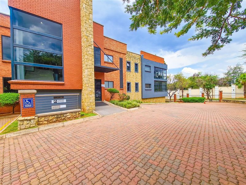 Front exterior view of a modern office building featuring a combination of brick and stone cladding, large glass windows, and a paved driveway.