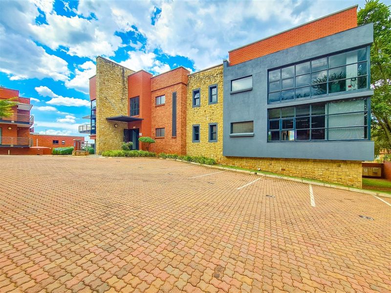 Modern office building exterior featuring a combination of stone and brick cladding, large glass windows, and a paved parking area.