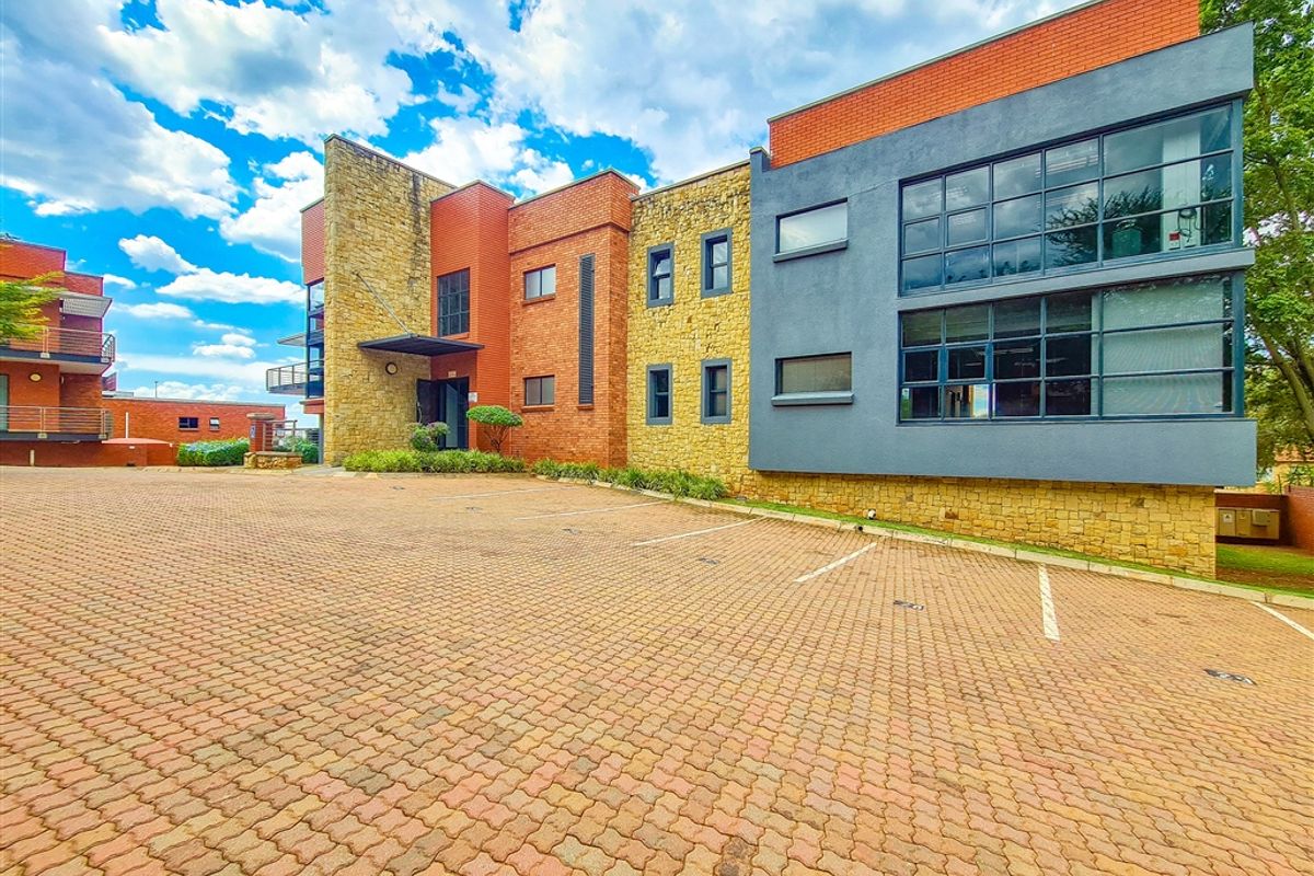 Modern office building exterior featuring a combination of stone and brick cladding, large glass windows, and a paved parking area.