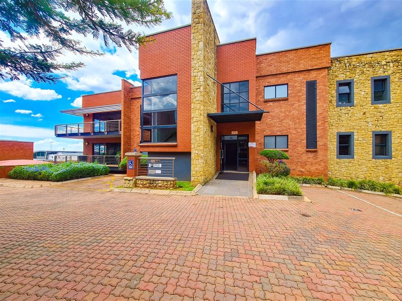 A professional office building exterior featuring a combination of red brick and stone cladding, with a paved driveway and accessible entrance ramp.