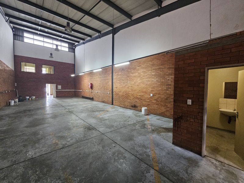 Spacious industrial warehouse unit featuring high ceilings, exposed brick walls, concrete flooring, and an integrated restroom facility.