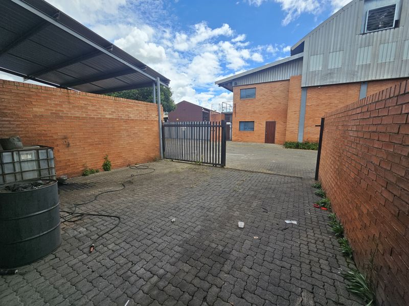 Industrial yard area featuring paved ground, brick boundary walls, a metal gate, and a covered storage section.