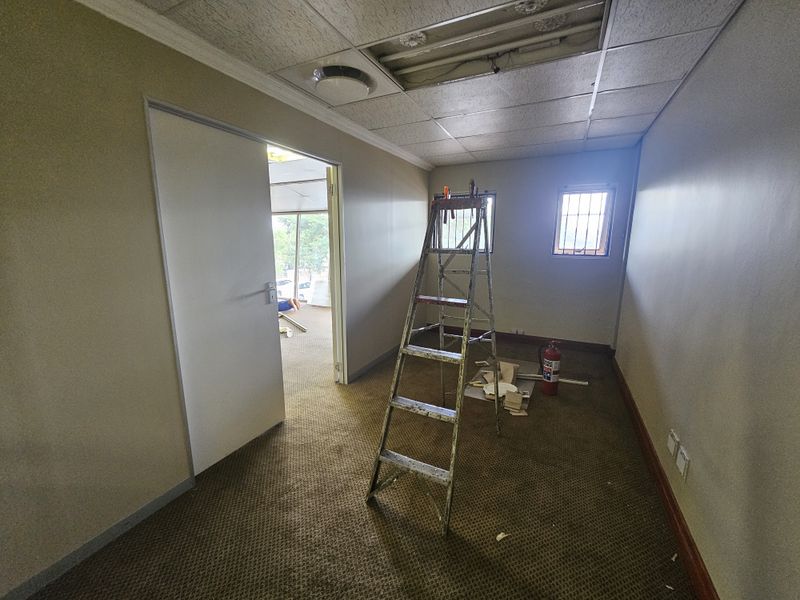 An office space featuring a drop ceiling, carpeted flooring, and security bars on the windows, currently undergoing maintenance.